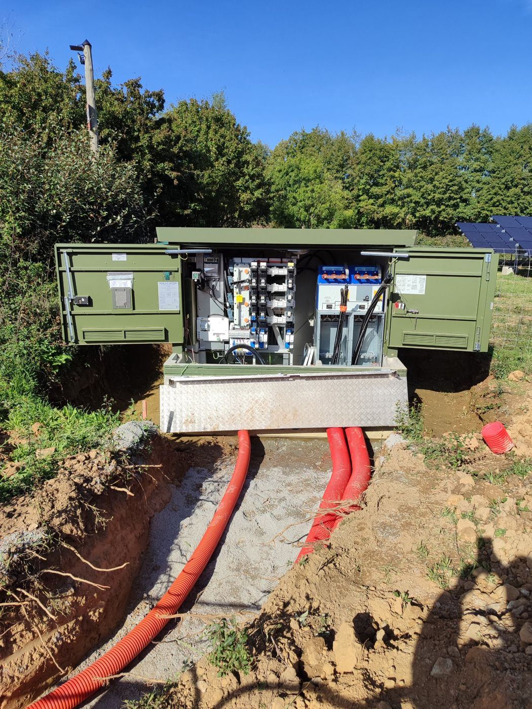 Poste de livraison de 250 kVA ouvert devant une centrale solaire au sol, gaines de raccordement en tranchée